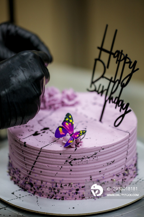 pastry chef topping lilac frosted birthday cake handmade with happy sign and butterfly