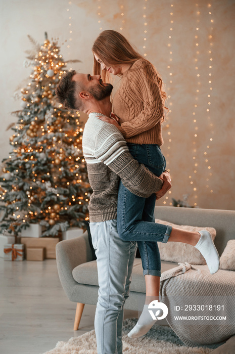 Man raised and holds the woman in his hands. Lovely young couple are celebrating New Year at home