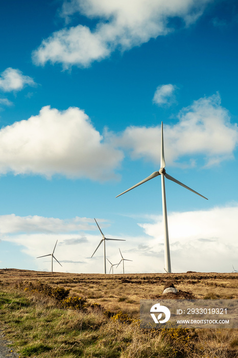 Wind electricity generators in an open field. Warm sunny day. Cloudy sky. Green power production concept. County Galway, Ireland.