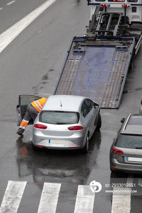 Scene of a broken down car on a city street road ready to load to the platform of flat bed tow truck