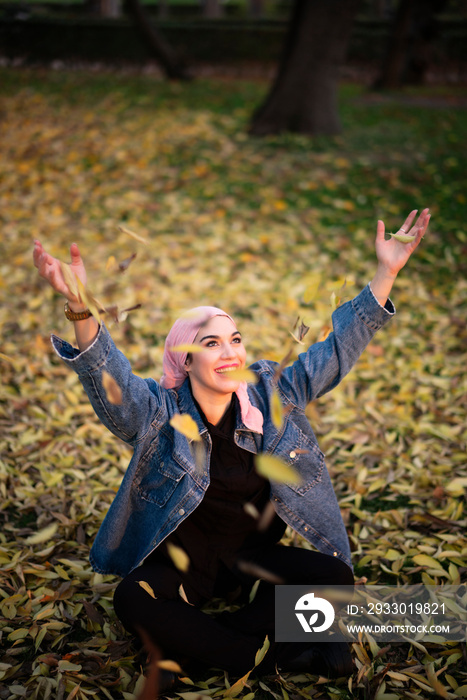 Young woman throws autumn leaves fighting cancer with pink scarf on her head