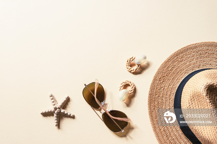 Flat lay with women’s summer accessories on neutral background. Sunglasses, straw hat, earrings and starfish. Summer travel concept. Top view, copy space