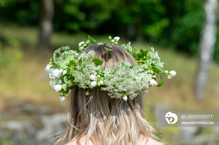 Woman with a flower wreath on her head. Midsummer celebration, a Swedish feast and tradition in June. Photography taken from behind, blurred bokeh background, copy space, place for text.