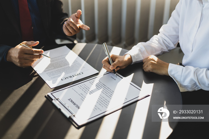 Businessman in suit in his office showing an insurance policy and pointing with a pen where the policyholder must to sign. Insurance agent presentation and consulting insurance detail to customer.