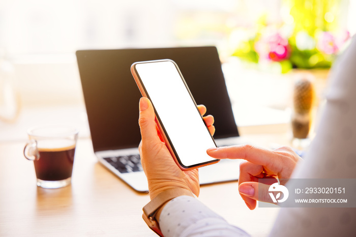 Woman working at her desk and holding mobile phone in hand with empty white screen