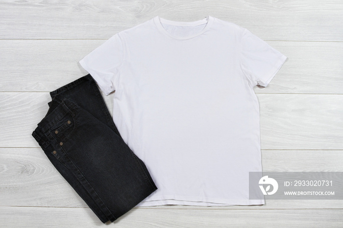 Closeup template blank white t shirt on wooden background. Top view, copy space summer t-shirt casual outfit. Black jeans. Front empty place for print and advertising