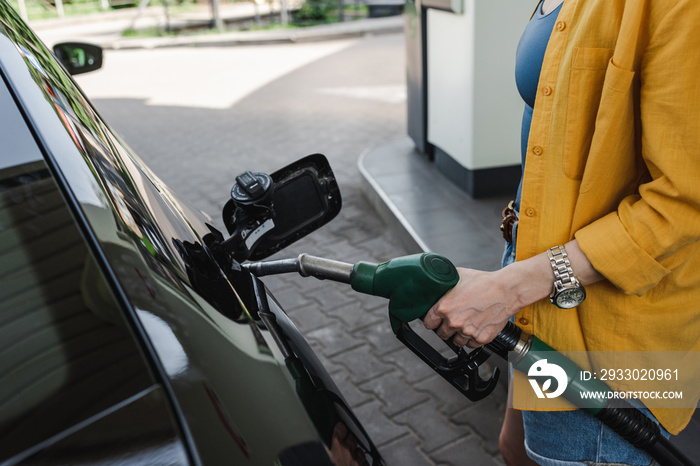 Cropped view of woman holding fueling nozzle near gas tank of car on urban street