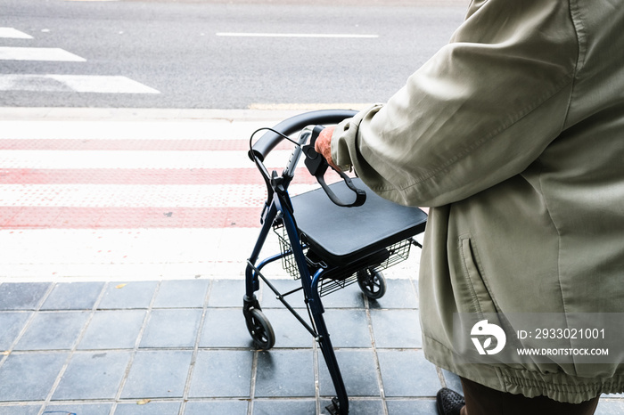 Elder waiting to cross a zebra crossing supported by a walker.