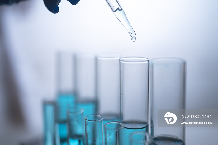 Closeup of hands of an unidentified person holding dropper pouring liquid or test sample in a tray of test tube in laboratory for testing and research work for investigation and invention