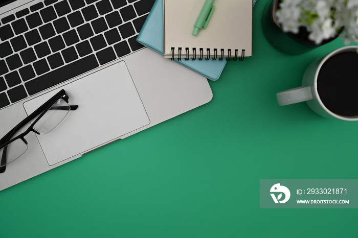 Above view computer laptop, eyeglasses, notebook and coffee cup on green background.