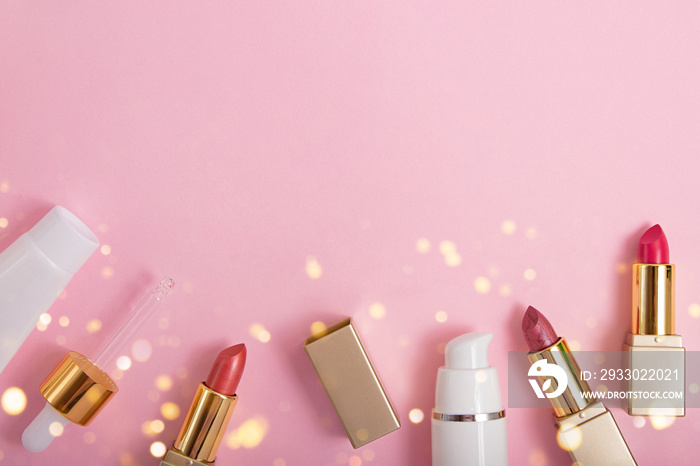 Top view of cosmetics containers and lipstick on pink background with shihing bokeh.Festive flat lay with copy space.