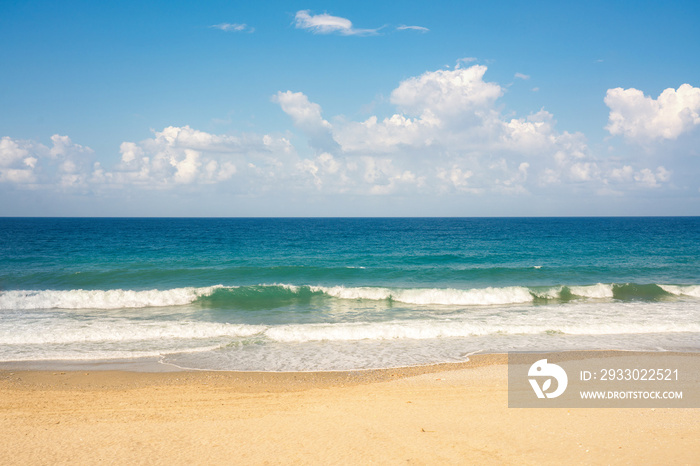 Colorful summer landscape with beautiful golden sandy beach with light rolling waves of turquoise sea against blue sky with clouds.