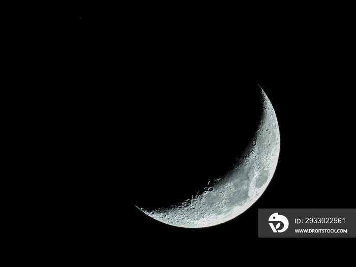 increasing sickle-shaped quarter moon with its moon craters stands in the black night sky