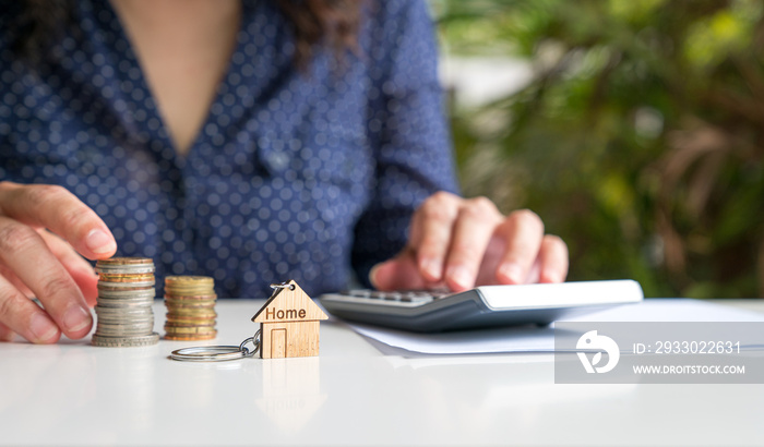 Home keychain with woman on calculator and coins at the background. Property valuation or investment concept.