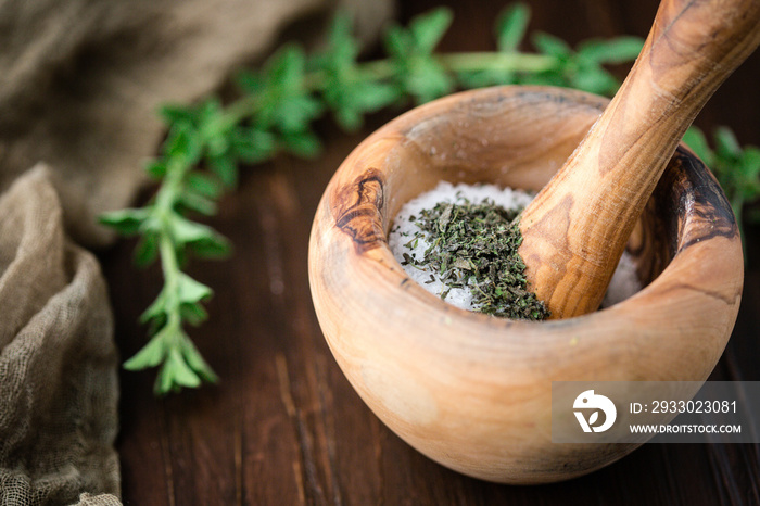 Dried Oregano in Mortar and Pestle to make Herb Salt with a fresh sprig of Oregano on a Wooden Table