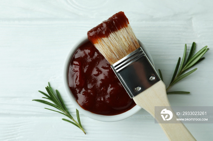 Bowl of barbecue sauce with brush and rosemary on white wooden table