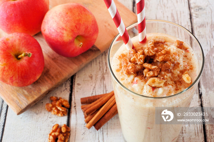 Apple pie smoothie close up in a glass with walnuts and cinnamon. Table scene against a white wood background.