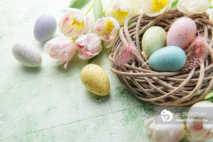 Nest with Easter eggs painted pastel colors on a green wooden background.