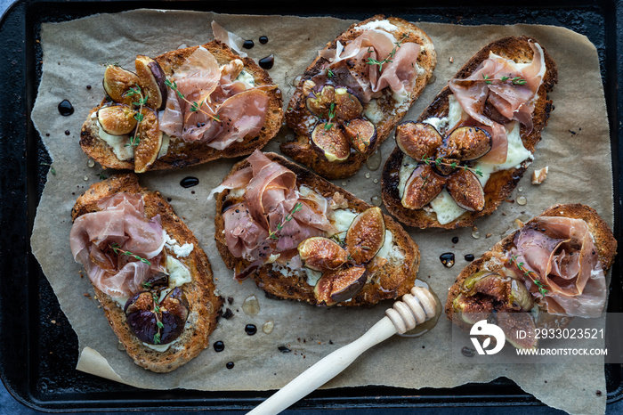 Toasted fig and prosciutto tartines on a parchment lined baking sheet.