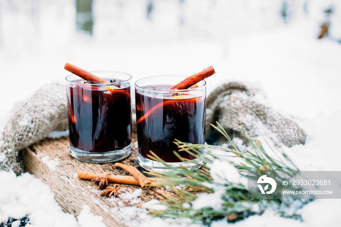 Mulled wine on a wooden board on a snowy table. Two glasses of hot wine with cinnamon and fresh vegetables..