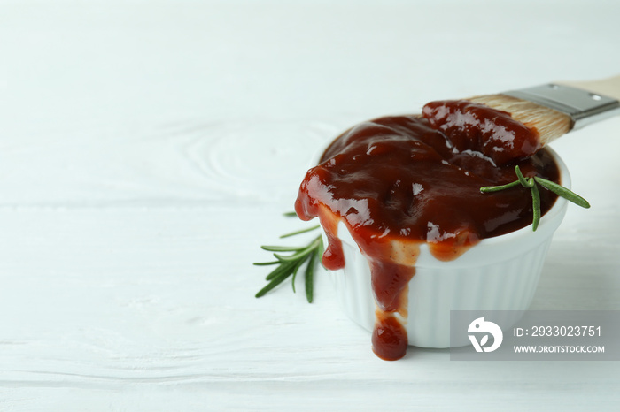 Bowl of barbecue sauce with brush and rosemary on white wooden table