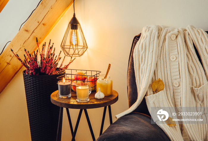 Cozy sick day at home. Table with hot tea cup, garlic and jar of honey. Cozy mood autumn season arrangement concept. Decorative lamp with decorative led bulb hanging on background. Hygge lifestyle.