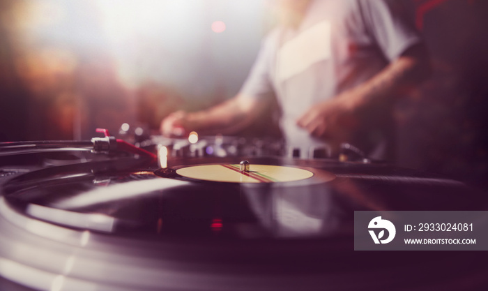 Dj plays music on party in night club. Vinyl record player on concert stage, silhouette of disc jockey in the background