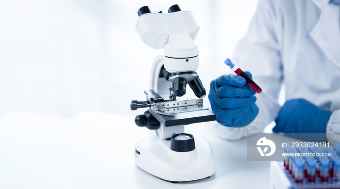 Doctor hand taking a blood sample tube from a rack with machines of analysis in the lab background, Technician holding blood tube test in the research laboratory.