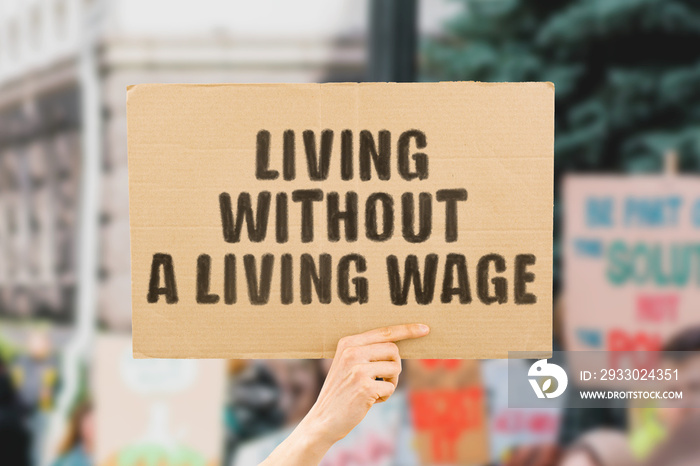 The phrase   Living without a living wage   on a banner in men’s hand. Human holds a cardboard with an inscription. Financial. Poorness. Money. Earnings. Revenue. Life. Social security. Economy