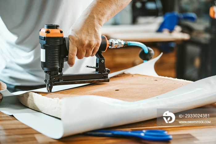 carpenter using  nail gun or staple gun after replace a vinyl or  upholstery fabric to the Seat for Bar Stools,furniture restoration woodworking concept. selective focus