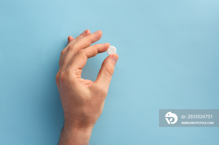 Male hand holding one pill. Flat lay.