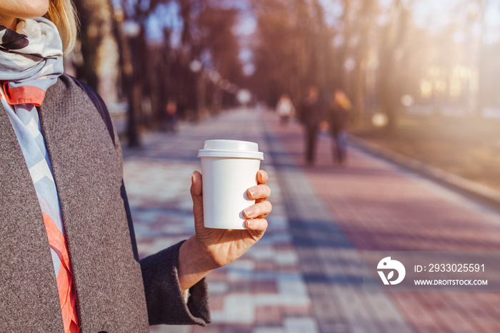 Young girl holding a coffee to take away for a walk in the park early in the morning, sunlight, blurred background.