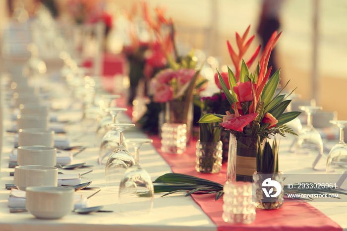 Close up dinner table tropical style set on the beach in sunset time Thailand. Beautiful delicate wedding decoration with tropical flowers and fruits. Wedding setting table on the beach.