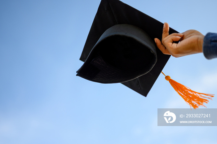 Graduates hold a black hat with a yellow tassel attached to the sky.