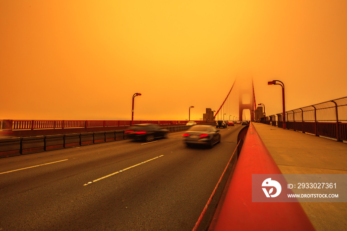 Cars crossing Golden Gate Bridge from Presidio to north. Smoky orange sky the bridge of San Francisco city for California fires in in America. Composition about wildfires and climate change concept.