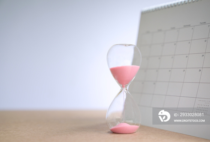 Hour glass with sand flowing on table, next to calendar