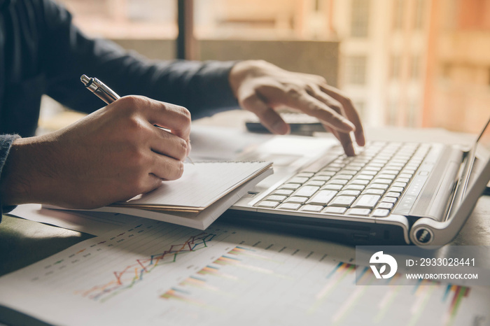 Close up hands man doing finances with using laptop and writing note at home office