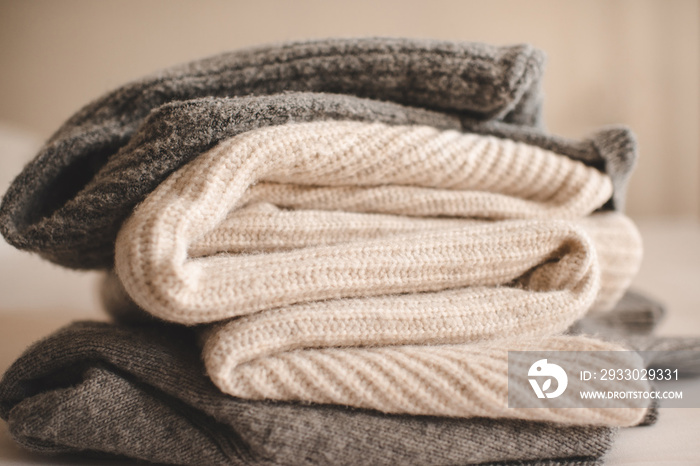 Stack of knitted wool textile sweaters clothes on white blanket in bed at home room close up. Winter cozy season.