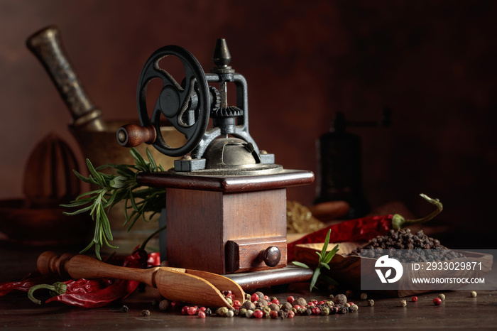 Vintage pepper mill with kitchen utensils, spices and rosemary on a old wooden table.