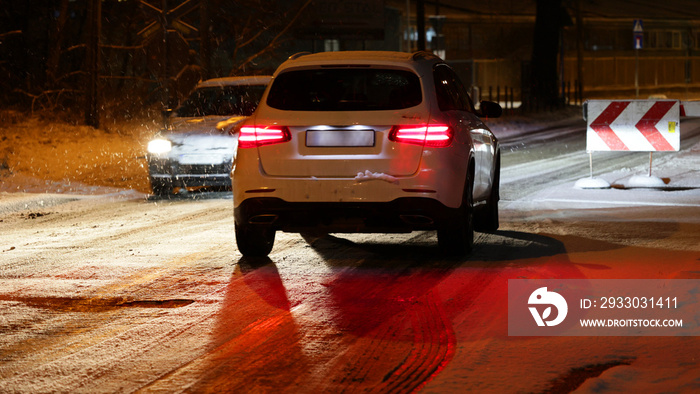 Pojazdy pług i piaskarka na drodze po nocnych opadach śniegu w mieście i ruch pojazdów.