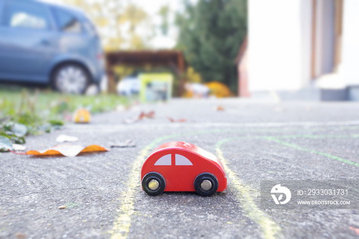 small red toy car in garden next to real vehicle