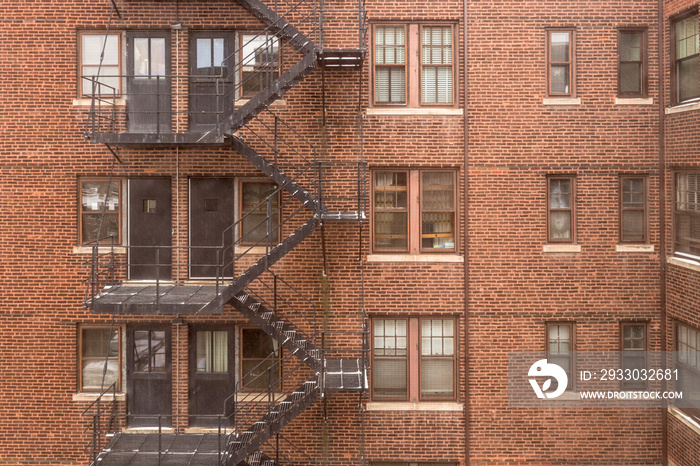 Side of vintage red brick apartment building with steel fire escape in large urban area