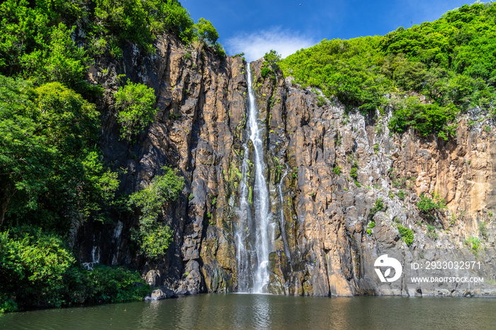 Rockface with waterfall Cascade Niagara at french island Reunion in the indian ocean on a sunny day with blue sky