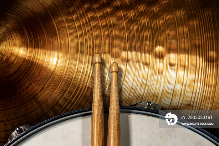 Close-up of two wooden drumsticks on an old metallic snare drum and golden colored cymbal with copy space. Percussion instrument