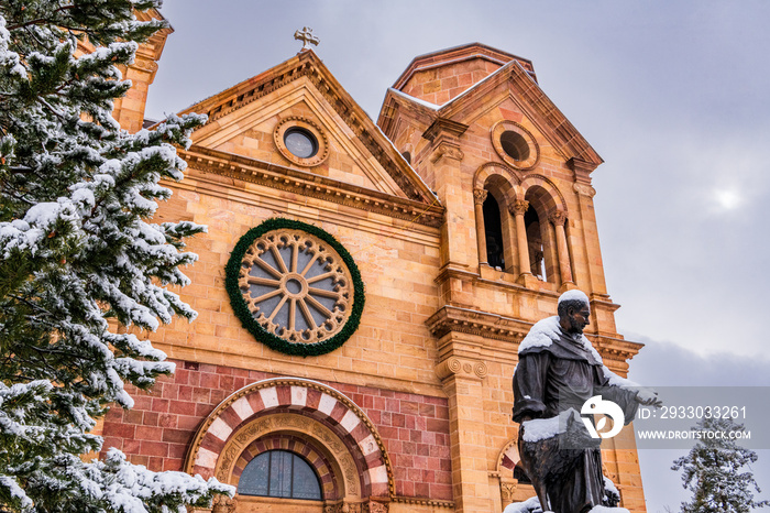 Snowy Christmas scene in Santa Fe, New Mexico, the Cathedral Basilica of Saint Francis with snow-covered tree, statue, and wreath