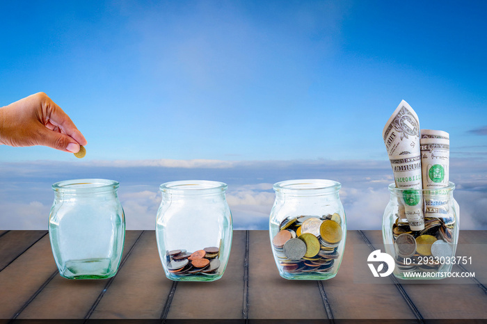 Saving  money. A hand putting money in bottle on sky and old wood background. The coins in the bottle for save money. Photo financial saving and  Saving  money.