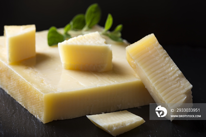 Matured cheese on dark slate with green oregano