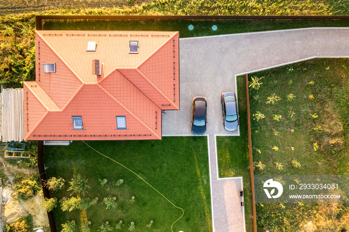 Top down aerial view of a private house with red tiled roof and spacious yard with parked two new cars.