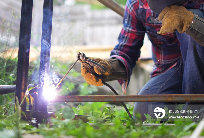 Man in a protective mask welding metal construction outside on a summer day