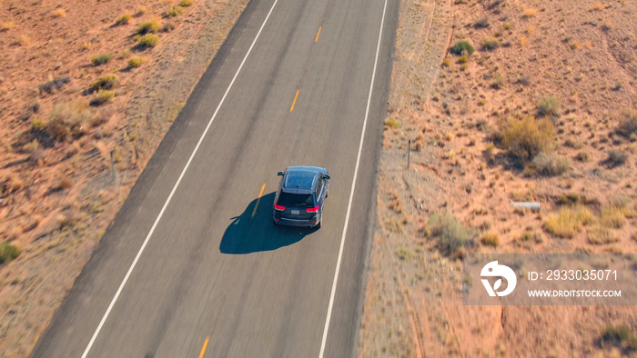 AERIAL CLOSE UP Flying above black SUV car driving on empty road in sandy desert